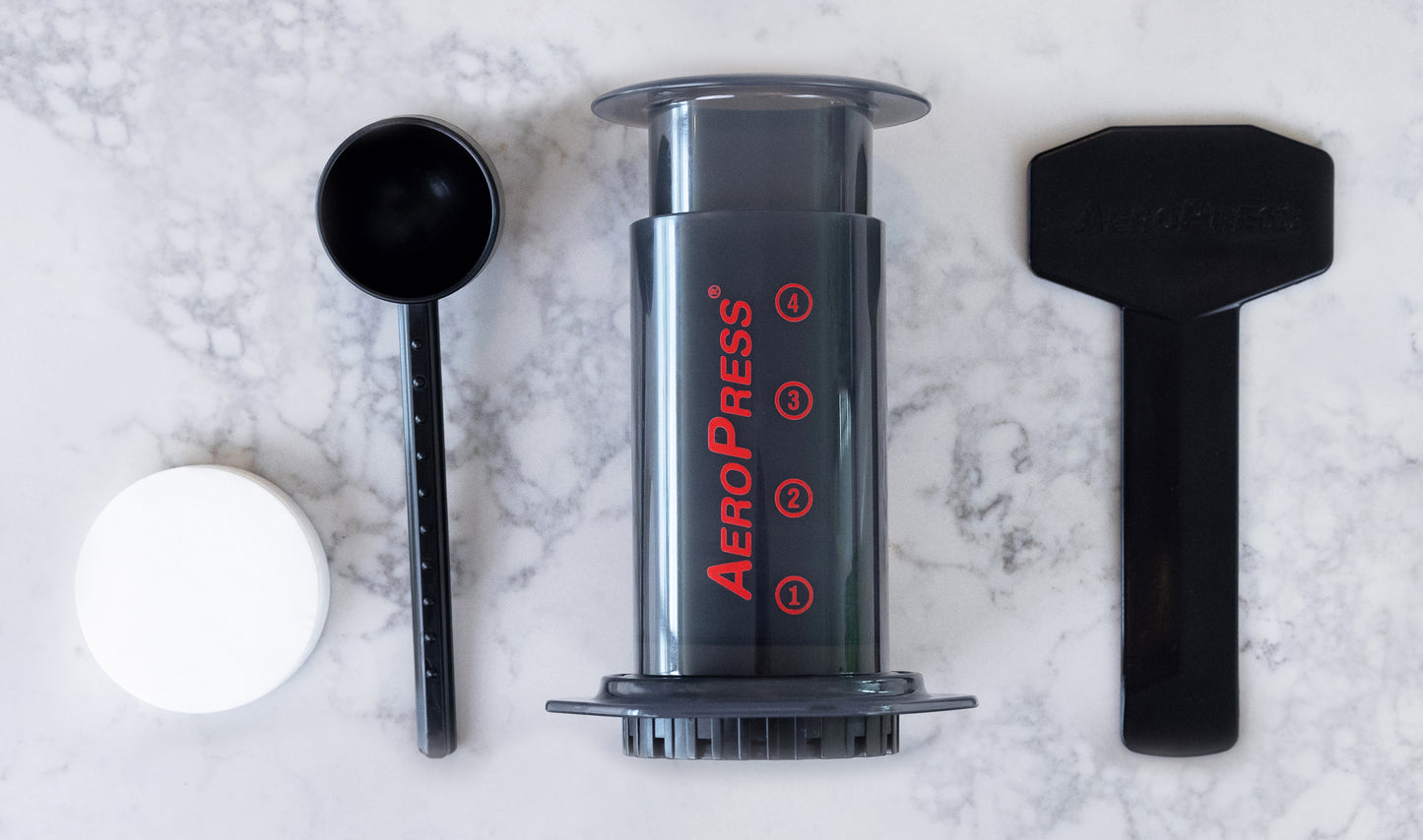 A black AeroPress Original Coffee Maker on a kitchen countertop laid out in a line to show parts